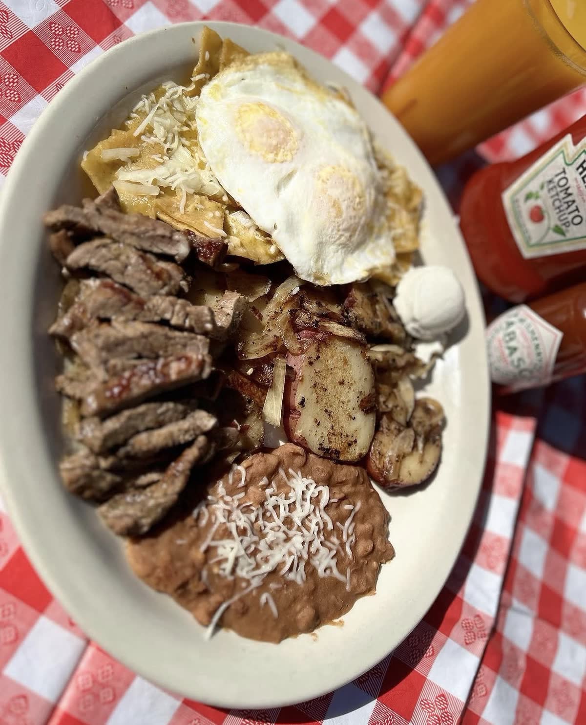 Chilaquiles with fajita steak, fried eggs, potatoes and beans on a red gingham tablecloth