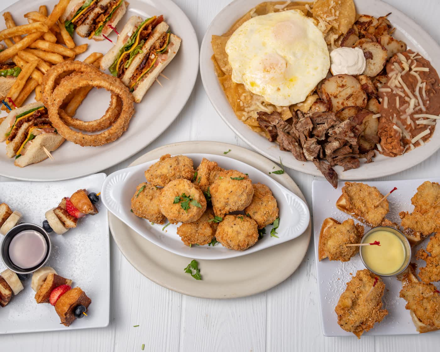 A spread of Belle's dishes: club sandwich with onion rings, chilaquiles with fajita steak and eggs, chicken and waffle bites, French toast skewers